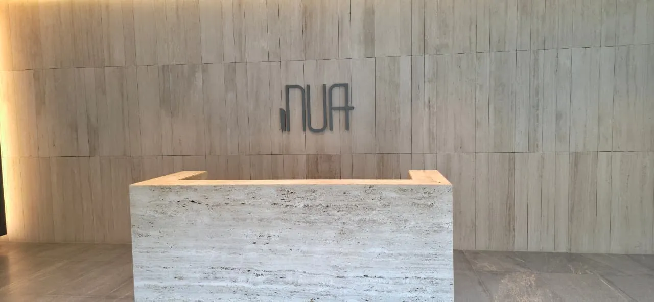 Recepción con muro de travertino y logo NUA — foto real